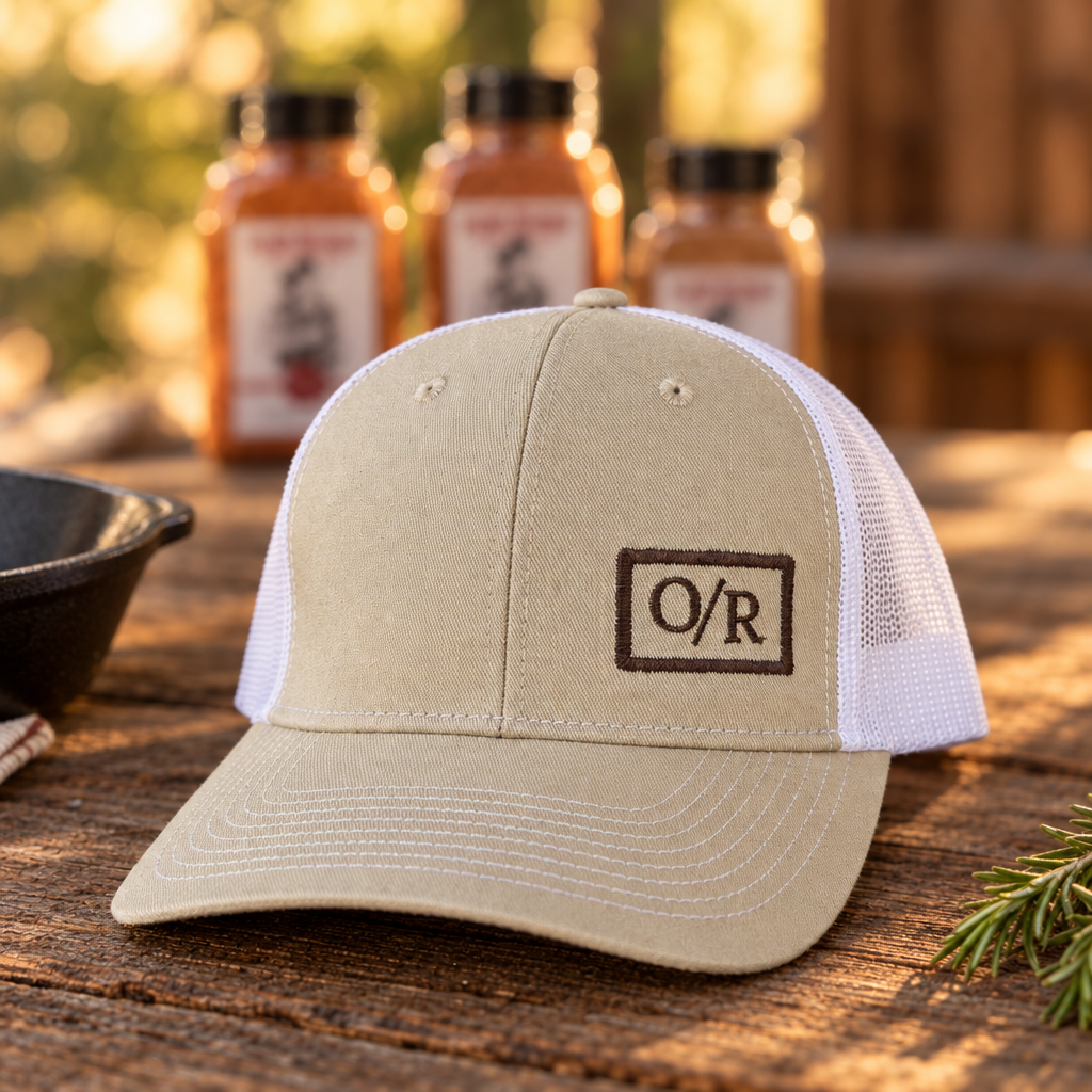 O/R trucker hat on a rustic wood table with Open Range spice jars behind it