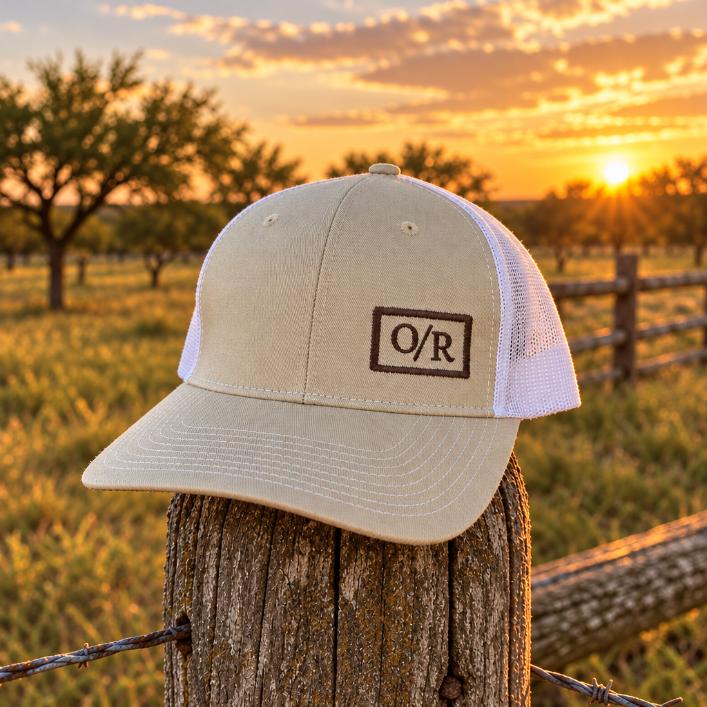 O/R trucker hat resting on a cedar fence post on a Texas ranch at sunset